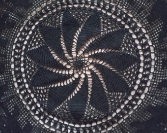 Pode incluir: Uma toalha de mesa redonda preta de crochê com um intrincado design de trabalho aberto. O centro apresenta um padrão em espiral, rodeado por motivos geométricos e florais. A toalha de mesa é feita de um fio escuro, possivelmente algodão.