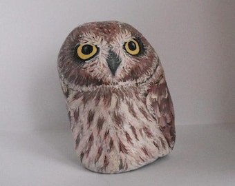 Pode incluir: Estatueta de coruja de pedra pintada à mão. A coruja tem olhos grandes amarelos, um bico escuro e penas castanhas e brancas. A estatueta é um item decorativo único.