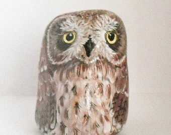 Pode incluir: Uma figura de coruja de pedra pintada à mão com detalhes castanhos, brancos e pretos. A coruja tem olhos amarelos e uma aparência realista.