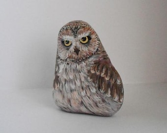 Pode incluir: Figurinha de coruja de pedra pintada à mão com detalhes realistas, com penas castanhas, brancas e cinzas, e olhos amarelos.