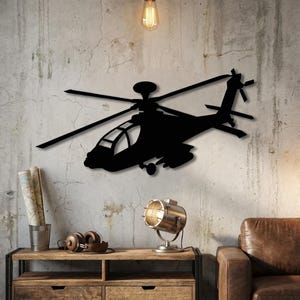 May include: Black metal helicopter wall art. The silhouette of the aircraft is mounted on a textured grey wall. The helicopter features a detailed design of the rotor blades, tail rotor, and cockpit. The wall art is a decorative piece for aviation enthusiasts.