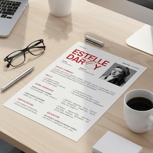 May include: A white ceramic mug with a black handle and the text "But First, Coffee" in a bold, black font. The mug is set against a blurred background, suggesting a cozy setting. The mug appears to be approximately 4 inches tall.