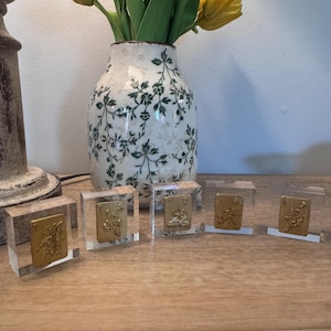 May include: A still life arrangement featuring a white vase with green floral patterns, holding yellow tulips. In front, five clear acrylic blocks display gold-colored playing cards, creating a decorative display.