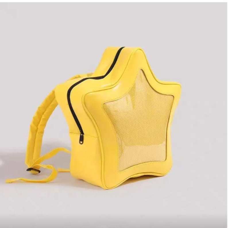 May include: A bright yellow star-shaped backpack featuring a clear, transparent front panel window. The bag includes a black zipper closure that outlines the star shape, along with matching yellow adjustable shoulder straps attached to the back.
