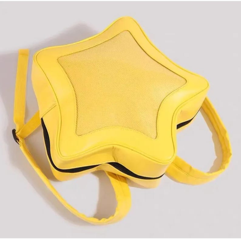 May include: A bright yellow star-shaped backpack featuring a textured central panel and smooth outer edges. The bag includes adjustable shoulder straps and a black zipper closure that follows the perimeter of the star shape, providing a structured design.