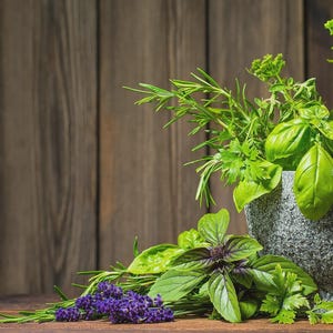 May include: A stone mortar and pestle filled with fresh herbs, including basil, rosemary, and lavender. The arrangement is set against a rustic wooden background, showcasing the vibrant green and purple hues of the ingredients.
