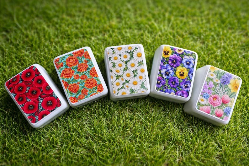 Peut inclure: Cinq bo&icirc;tes rectangulaires d&eacute;coratives avec des motifs floraux : coquelicots rouges, soucis oranges, marguerites blanches, pens&eacute;es violettes et roses roses. Les bo&icirc;tes ont des bordures blanches, sur de l'herbe verte.