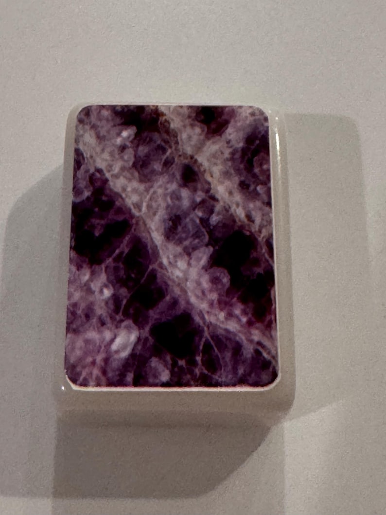 May include: A rectangular object with a marbled purple and white design. The object has a white border and a smooth, glossy finish. The design resembles amethyst or other natural stone.