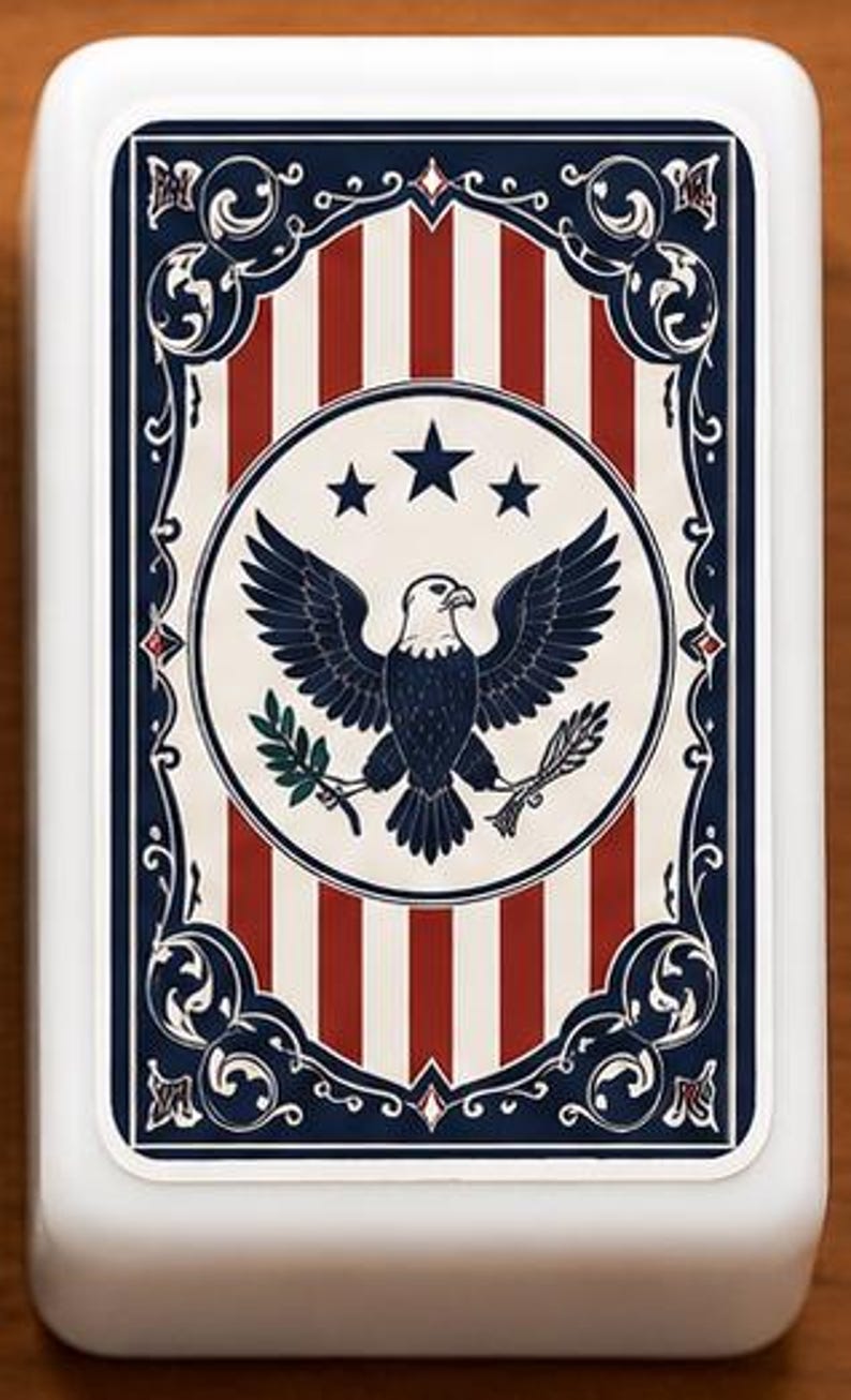 May include: A white rectangular box with a patriotic design. The design features red and white stripes, a circular emblem with an eagle, stars, and a blue border with decorative elements. The overall theme is Americana.