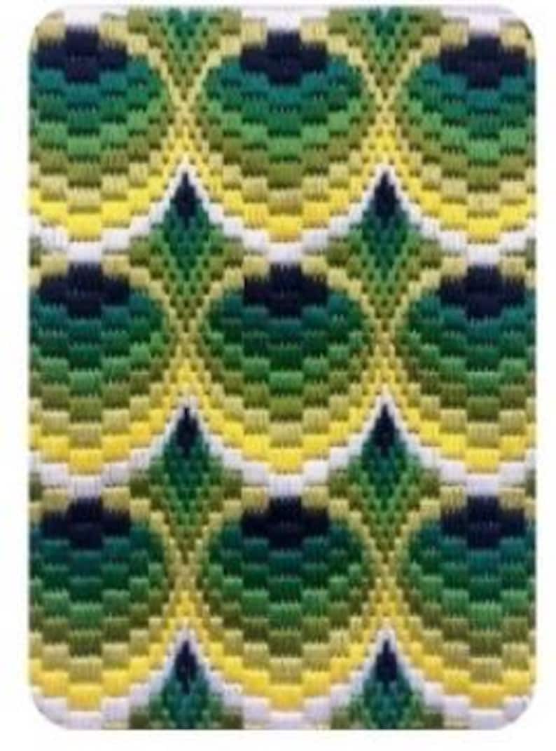 May include: A rectangular patch with a repeating pattern of green, yellow, and white embroidered shapes. The design features a series of interconnected, stylized peacock feather motifs. The patch has a white border and a textured appearance.