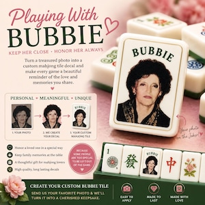 May include: A custom mahjong tile featuring a portrait of a woman with dark hair and the text BUBBIE printed above her image. The tile is white with a gold border, displayed alongside other standard mahjong tiles in a green rack and on a surface.