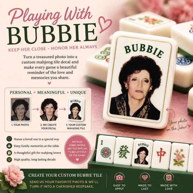 May include: A custom mahjong tile featuring a portrait of a woman with dark hair and the text BUBBIE printed above her image. The tile is white with a gold border, displayed alongside other standard mahjong tiles in a green rack and on a surface.