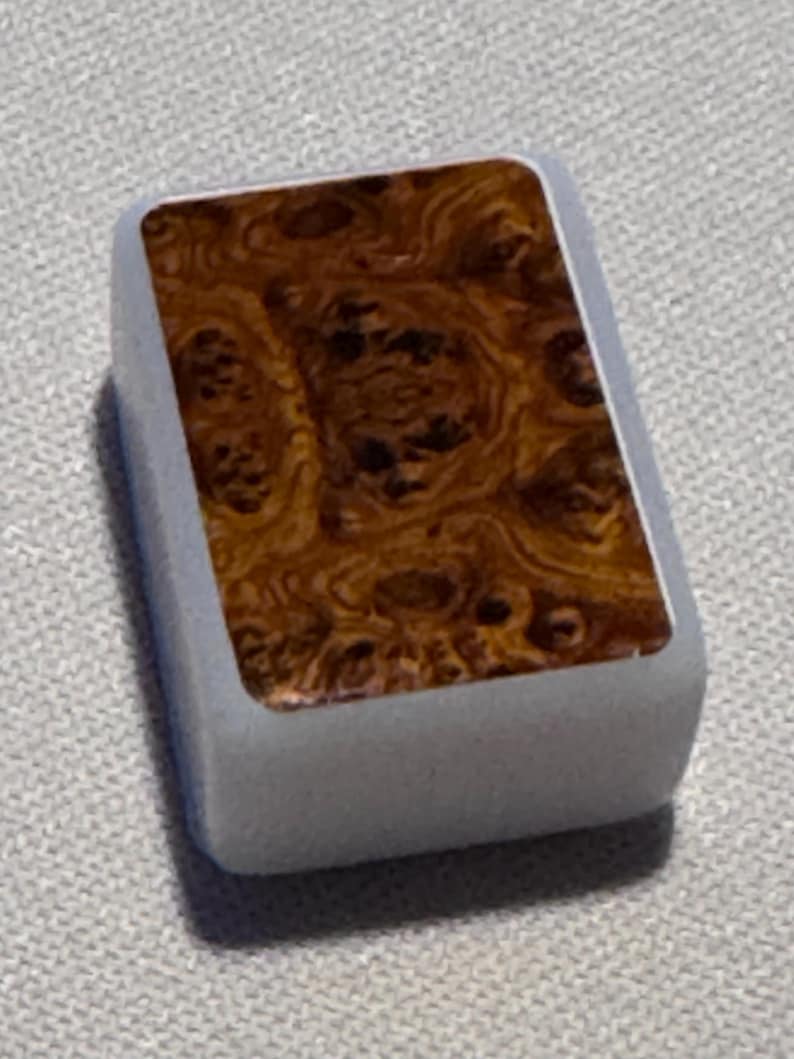 Op de afbeelding: Een rechthoekig, lichtgrijs object met een houtnerfpatroon op het bovenoppervlak. De houtnerf heeft wervelingen van bruin en beige. Het object heeft afgeronde randen en een gladde afwerking.