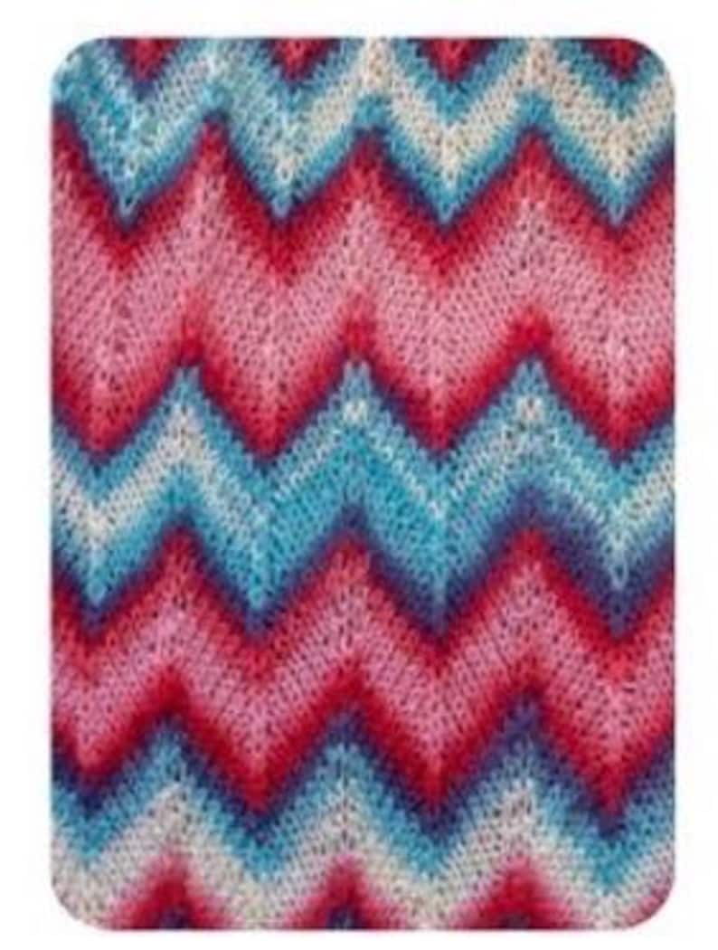May include: A rectangular knitted fabric with a chevron pattern. The design features alternating bands of red, pink, light blue, and white. The fabric has a textured appearance, suggesting a soft and comfortable material.