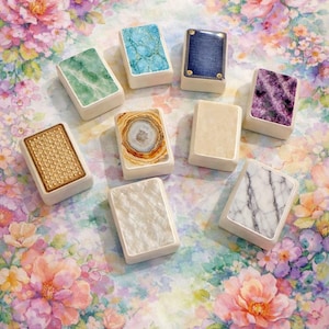 Może przedstawiać: Kolekcja prostokątnych przedmiotów dekoracyjnych z różnymi wzorami, w tym marmurem i agatem. Ułożone na kwiatowym tle w odcieniach różu, fioletu i zieleni.