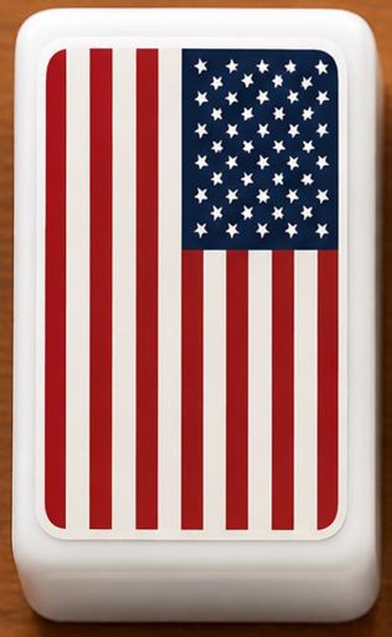 May include: A white, rectangular object with rounded corners. The top surface displays a printed design of the American flag, with red and white stripes and a blue field with white stars. The object is likely a container or decorative item.