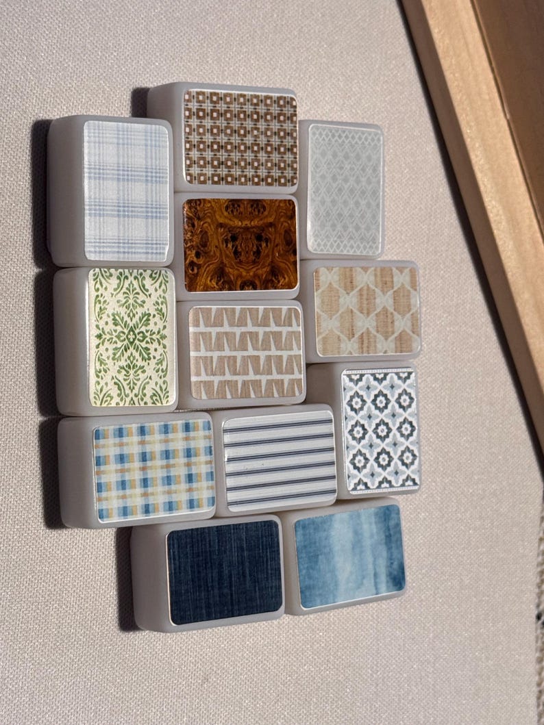 Op de afbeelding: Een verzameling rechthoekige tegels met diverse decoratieve patronen. De patronen omvatten ruitjes, bloemen, houtnerf en geometrische ontwerpen in blauw, bruin en wit. De tegels zijn in een cluster gerangschikt.