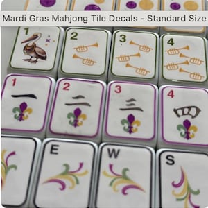 Peut inclure: Gros plan sur plusieurs tuiles de Mahjong blanches avec des d&eacute;calcomanies sur le th&egrave;me du Mardi Gras. Les tuiles pr&eacute;sentent des chiffres, des trompettes et des motifs de fleur de lys en vert, violet et or. Le texte "Mardi Gras Mahjong Tile Decals - Standard Size" est visible.