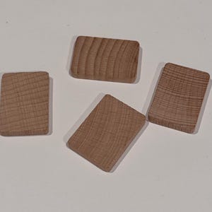 Puede incluir: Cuatro bloques de madera rectangulares con esquinas redondeadas. Los bloques son de color marr&oacute;n claro y muestran la veta natural de la madera. Los bloques est&aacute;n dispuestos sobre una superficie blanca.