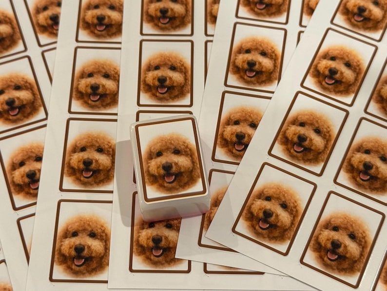 May include: A rectangular rubber stamp featuring a custom portrait of a golden-brown curly-haired dog with a smiling expression, positioned on top of several sheets of matching stickers that display the same dog portrait in a brown-bordered frame.