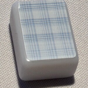 Op de afbeelding: Een lichtgrijs, rechthoekig object met een blauw-wit ruitpatroon op het bovenvlak. Het object heeft afgeronde randen en lijkt gemaakt van een glad, stevig materiaal. Het ruitpatroon heeft een raster van elkaar kruisende lijnen.