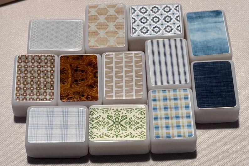 Op de afbeelding: Een verzameling rechthoekige tegels met diverse decoratieve patronen. Ontwerpen omvatten geometrische vormen, houtnerf, strepen en bloemmotieven. De tegels zijn in tinten blauw, bruin, beige en wit.