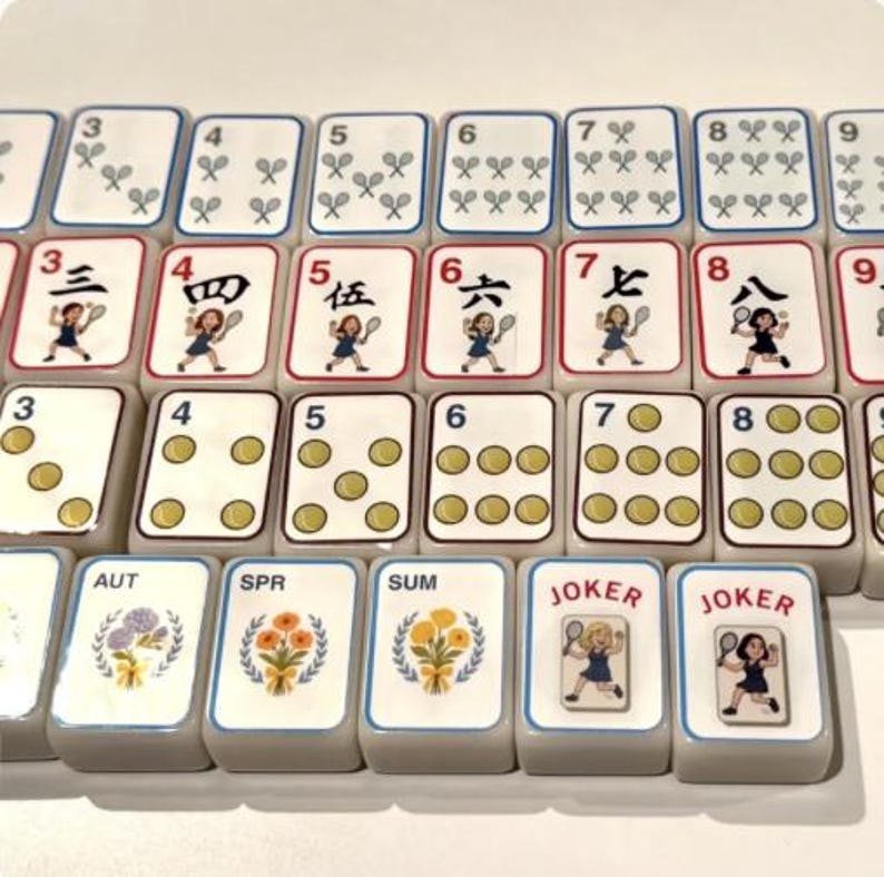 Peut inclure: Un ensemble de tuiles de Mahjong, pr&eacute;sentant divers symboles, chiffres et caract&egrave;res. Les tuiles sont blanches avec des accents rouges, bleus et dor&eacute;s. Certaines tuiles affichent des joueurs de tennis, d'autres des motifs floraux et le mot "JOKER".