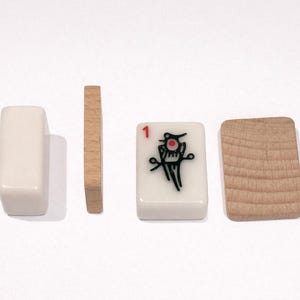 Puede incluir: Cuatro fichas de Mahjong se muestran sobre un fondo blanco. Dos son rectangulares y blanquecinas, dos son de madera. Una ficha tiene un '1' rojo y un gr&aacute;fico negro y rojo. Las fichas de madera tienen un patr&oacute;n de vetas.