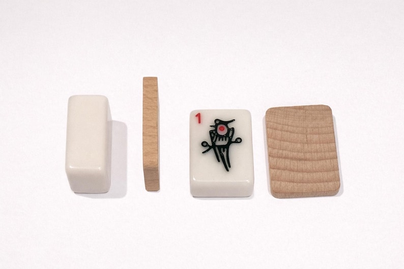 Puede incluir: Cuatro fichas de Mahjong se muestran sobre un fondo blanco. Dos son rectangulares y blanquecinas, dos son de madera. Una ficha tiene un '1' rojo y un gr&aacute;fico negro y rojo. Las fichas de madera tienen un patr&oacute;n de vetas.
