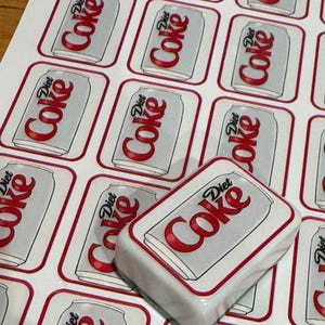 May include: Sheet of stickers featuring a Diet Coke can design. The stickers are rectangular with a white background and a red border. The Diet Coke logo is prominently displayed on each sticker.