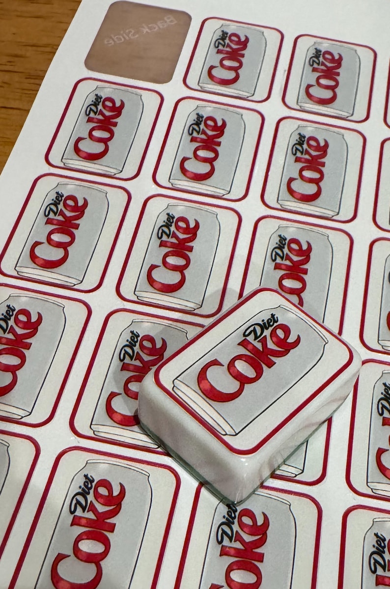 May include: Sheet of stickers featuring a Diet Coke can design. The stickers are rectangular with a white background and a red border. The Diet Coke logo is prominently displayed on each sticker.