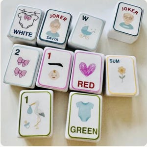 Peut inclure: Un ensemble de tuiles blanches rectangulaires avec diverses illustrations et du texte. Les tuiles pr&eacute;sentent des images de b&eacute;b&eacute;, de n&oelig;uds, d'une cigogne et d'un body, ainsi que les mots "WHITE", "RED" et "GREEN". Certaines tuiles ont le mot "JOKER" et une image d'une personne.