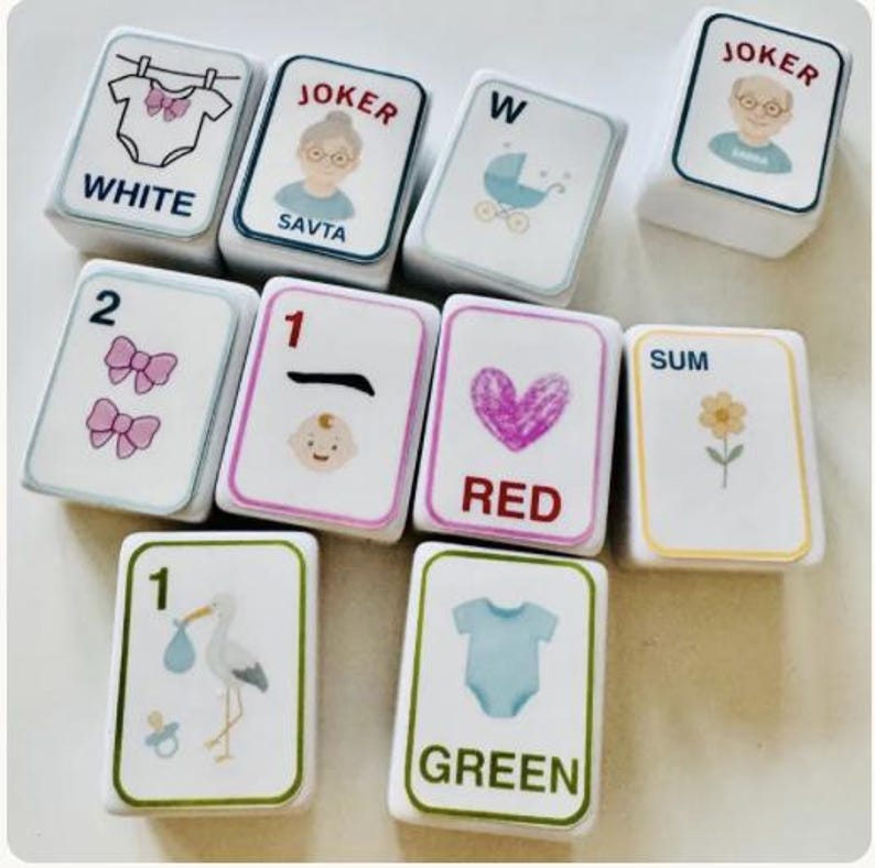 Peut inclure: Un ensemble de tuiles blanches rectangulaires avec diverses illustrations et du texte. Les tuiles pr&eacute;sentent des images de b&eacute;b&eacute;, de n&oelig;uds, d'une cigogne et d'un body, ainsi que les mots "WHITE", "RED" et "GREEN". Certaines tuiles ont le mot "JOKER" et une image d'une personne.