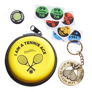 Puede incluir: Una caja redonda amarilla con una cremallera negra y el texto "I am a tennis ace" impreso en ella. La caja está al lado de un llavero dorado con un diseño de raqueta de tenis y el texto "so I can play tennis".