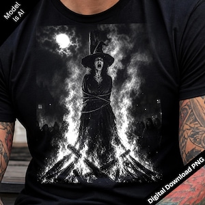 Op de afbeelding: Een zwart t-shirt met een grafische print van een persoon met een puntmuts vastgebonden aan een houten paal, omringd door vlammen en rook onder een volle maan. Het ontwerp bevat een menigte op de achtergrond, weergegeven in zwart-wit.
