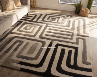 May include: A rectangular area rug with a geometric pattern in shades of gray, black, and beige. The design features interlocking squares and lines. The rug is placed on a hardwood floor in a living room setting. The text "Weavers Dream Rugs" is visible.