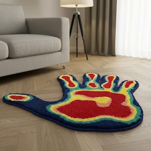 Puede incluir: Una alfombra con forma de mano con un fondo azul y un diseño de mapa de calor colorido en rojo, amarillo y verde. La alfombra está colocada sobre un suelo de madera cerca de un sofá gris y una lámpara.