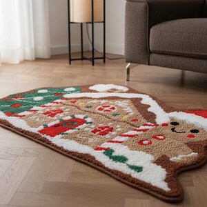 Puede incluir: Una alfombra caprichosa con forma de hombre de jengibre con un diseño festivo. La alfombra presenta una base marrón con detalles de glaseado blanco, detalles rojos y verdes y un gorro de Papá Noel. Está colocada sobre un suelo de madera.