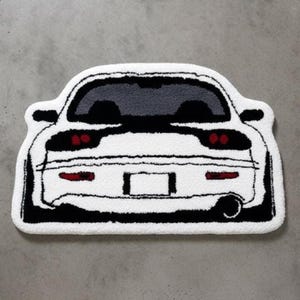 May include: White car-shaped rug with black and red accents. The rug features a detailed outline of a car's rear, including taillights, a license plate area, and a single exhaust pipe. The car's windows are gray.