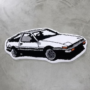 Può includere: Un tappeto a forma di auto bianca e nera con dettagli arancioni. Il tappeto presenta un design dettagliato di un'auto sportiva classica, con ruote nere e sottoscocca nero. La carrozzeria dell'auto è bianca con dettagli neri.