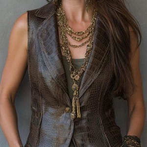 May include: A sleeveless brown vest with a textured crocodile skin pattern, featuring a notched lapel and a single button closure. The vest is layered over a dark olive top and accessorized with a multi-strand gold chain necklace and tassel.