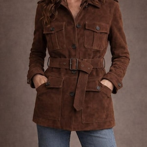 Könnte beinhalten: Braune Wildlederjacke mit Taillengürtel, Knopfverschlüssen und mehreren Taschen. Die Jacke hat ein klassisches Design und wird mit blauen Jeans kombiniert. Ein stilvolles Oberbekleidungsstück.