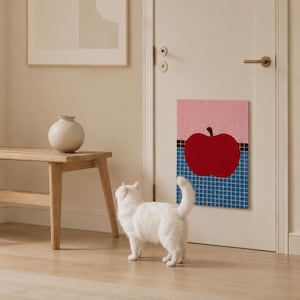 May include: A rectangular wall hanging featuring a graphic illustration of a solid red apple centered against a background of pink and blue grid patterns, mounted on a white door. The artwork displays a distinct contrast between the red fruit and the blue tiled grid base, with a soft pink upper section.
