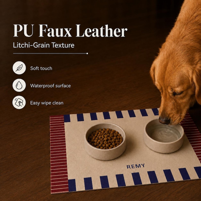 May include: A rectangular pet feeding mat made of PU faux leather with a litchi-grain texture. The mat features a beige center with the name REMY printed in blue, bordered by blue stripes and red striped edges. Two round bowls sit on the mat.