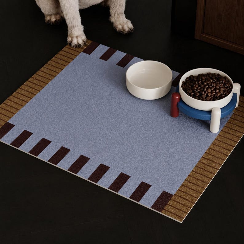 May include: A square pet feeding mat with a textured light blue center, brown striped borders, and dark brown rectangular accents. Two white ceramic bowls sit on the mat, one empty and one filled with brown dry kibble on a blue stand.