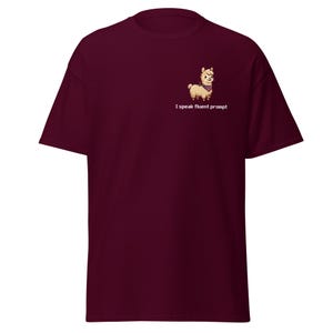 Könnte beinhalten: Ein kastanienbraunes T-Shirt mit kurzen Ärmeln und einer kleinen Pixel-Art-Grafik auf der linken Brust. Das Motiv zeigt ein hellbraunes Lama mit einem dunkelvioletten Halstuch sowie den weißen, verpixelten Text I speak fluent prompt.