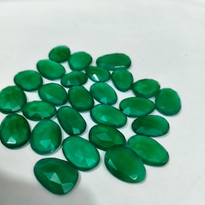 Peut inclure: Un ensemble de pierres précieuses vertes, taillées en forme ovale et à facettes. Les pierres polies varient légèrement en taille et en forme, avec une couleur verte émeraude vibrante. Les pierres sont disposées sur une surface blanche.