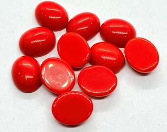 May include: A collection of eleven polished, oval-shaped, bright red gemstones. The stones are arranged in a loose cluster, each with a smooth, glossy surface. The gemstones are likely for jewelry making or crafting.