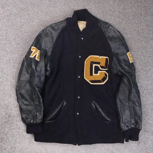May include: A vintage black varsity jacket with leather sleeves. The jacket has a large gold "C" patch on the chest and gold numbers on the sleeves. It features a button-up front and two front pockets.