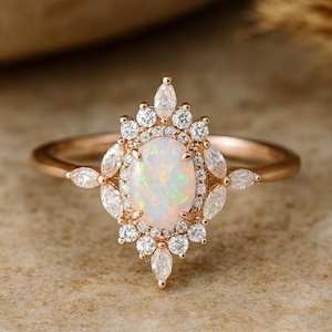 Könnte beinhalten: Roségoldener Ring mit einem ovalen Opal-Mittelstein, umgeben von kleinen runden und marquiseförmigen Diamanten. Das Ringband ist aus zartem Roségold, was ein elegantes und auffälliges Design ergibt. Ein wunderschönes Schmuckstück.
